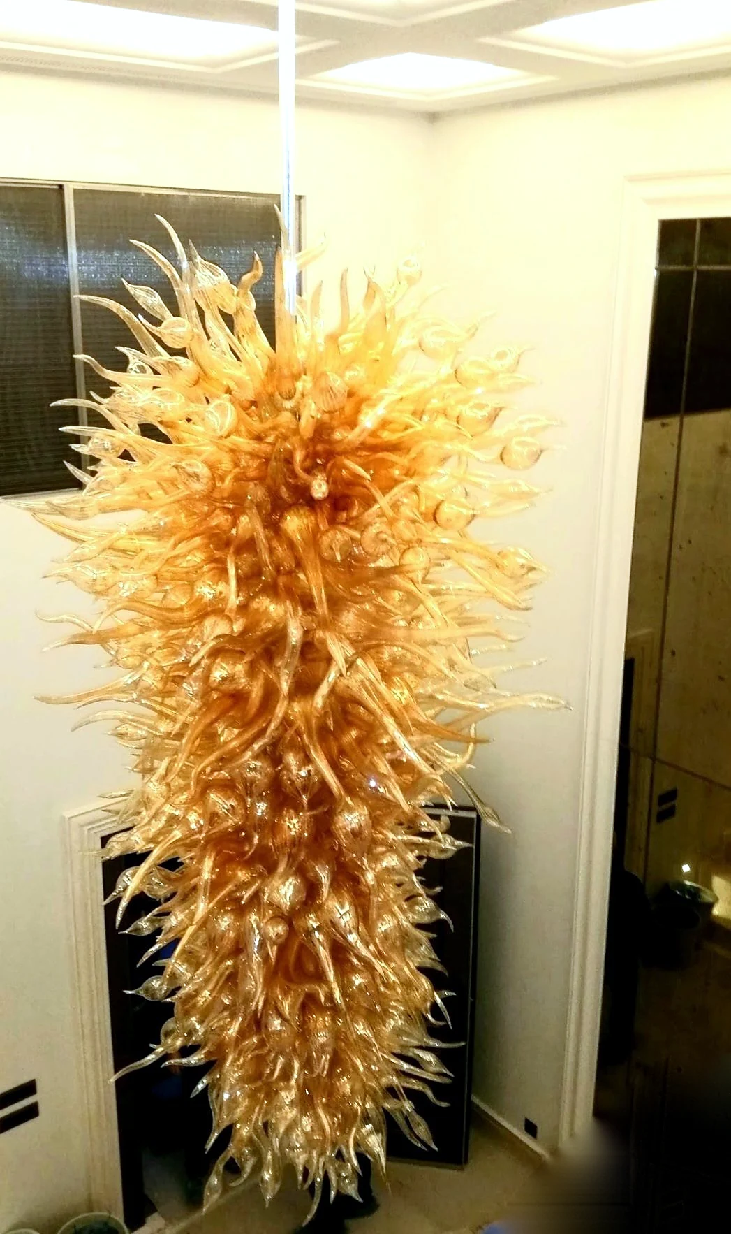 Large golden amber glass petal cascade chandelier suspended in a pale interior