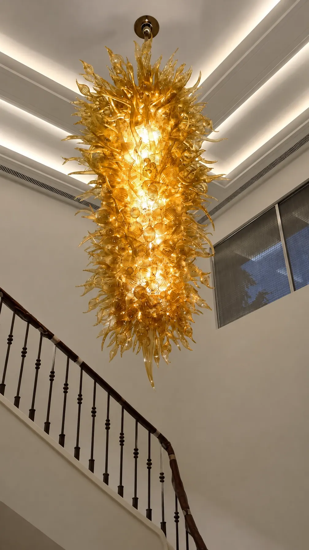 Large illuminated gold glass chandelier cascading through a stairwell