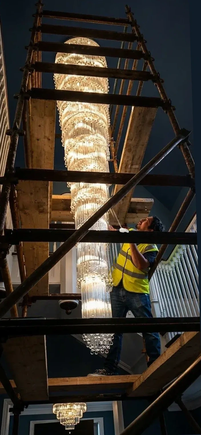 Chandelier specialist in a high-visibility vest working beside a tall cascade chandelier from access scaffolding