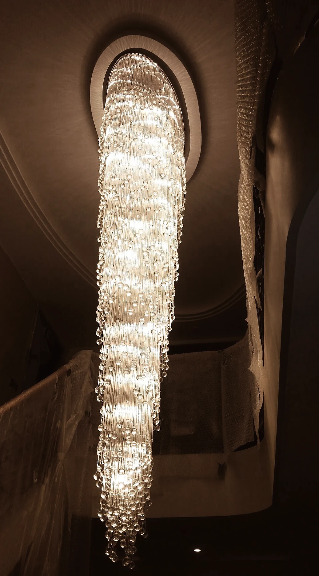 Tall illuminated crystal rod cascade chandelier beneath its oval ceiling rose
