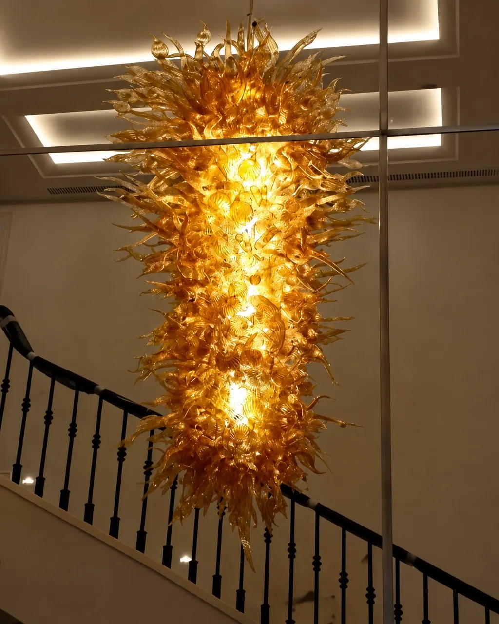 Illuminated gold glass chandelier cascading above a staircase