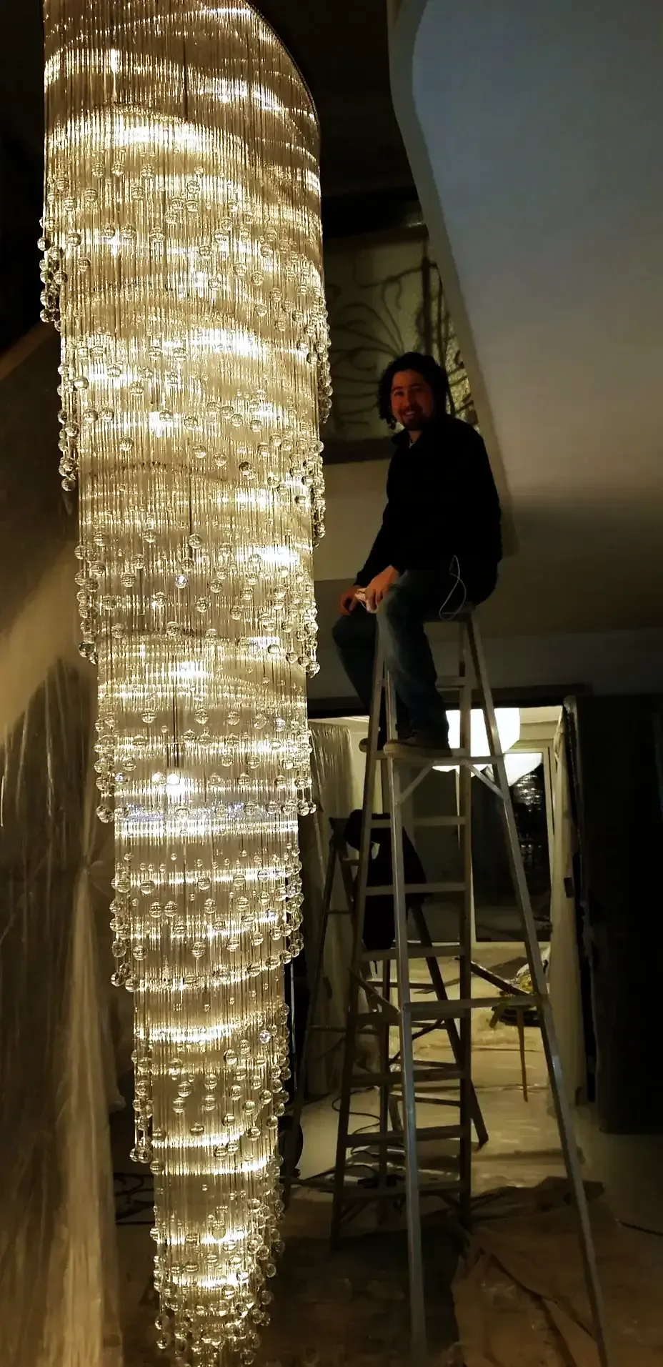 Chandelier specialist on a stepladder beside a tall crystal rod cascade chandelier