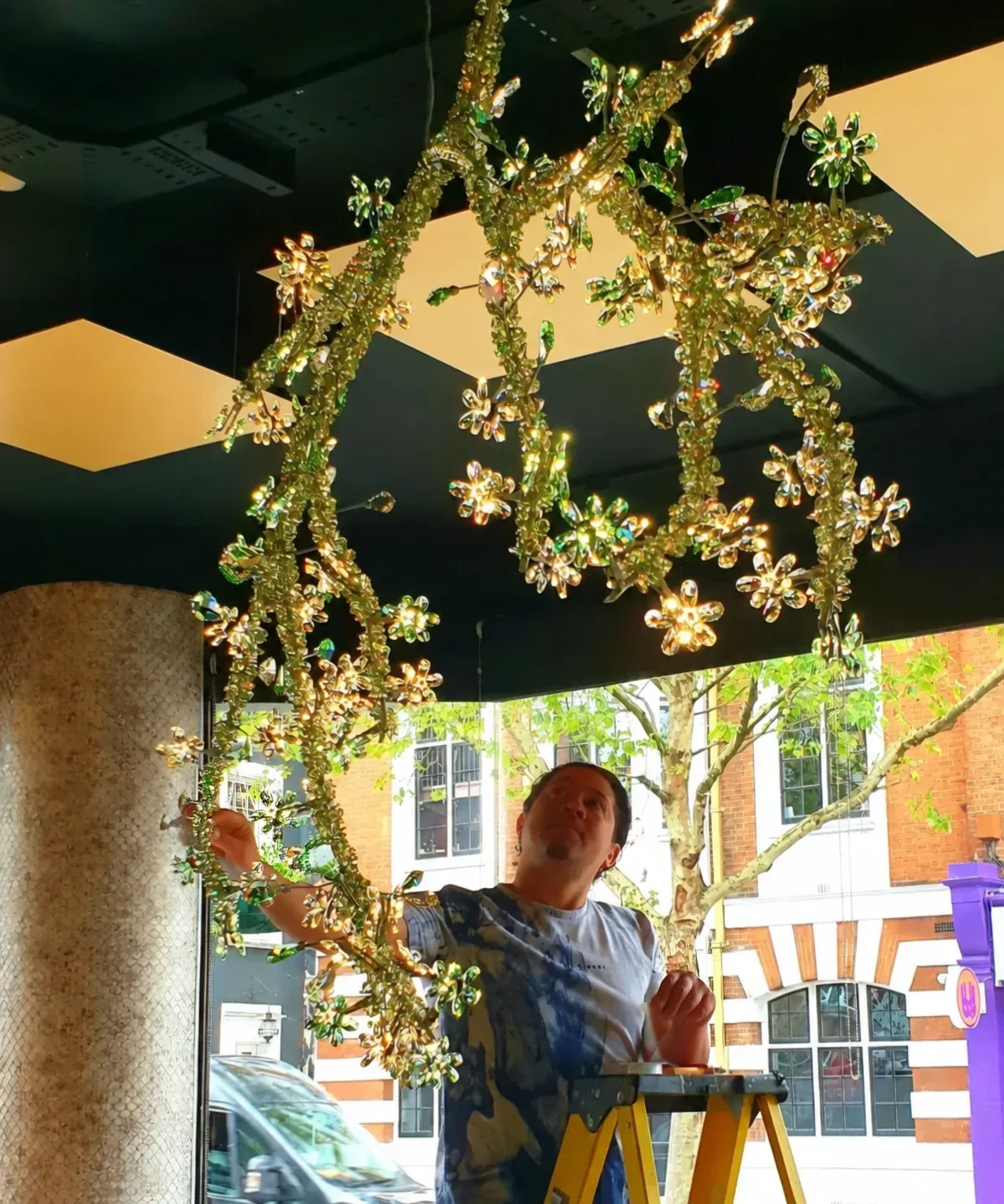 Specialist in a safety vest adjusting a gold and green crystal chandelier during installation