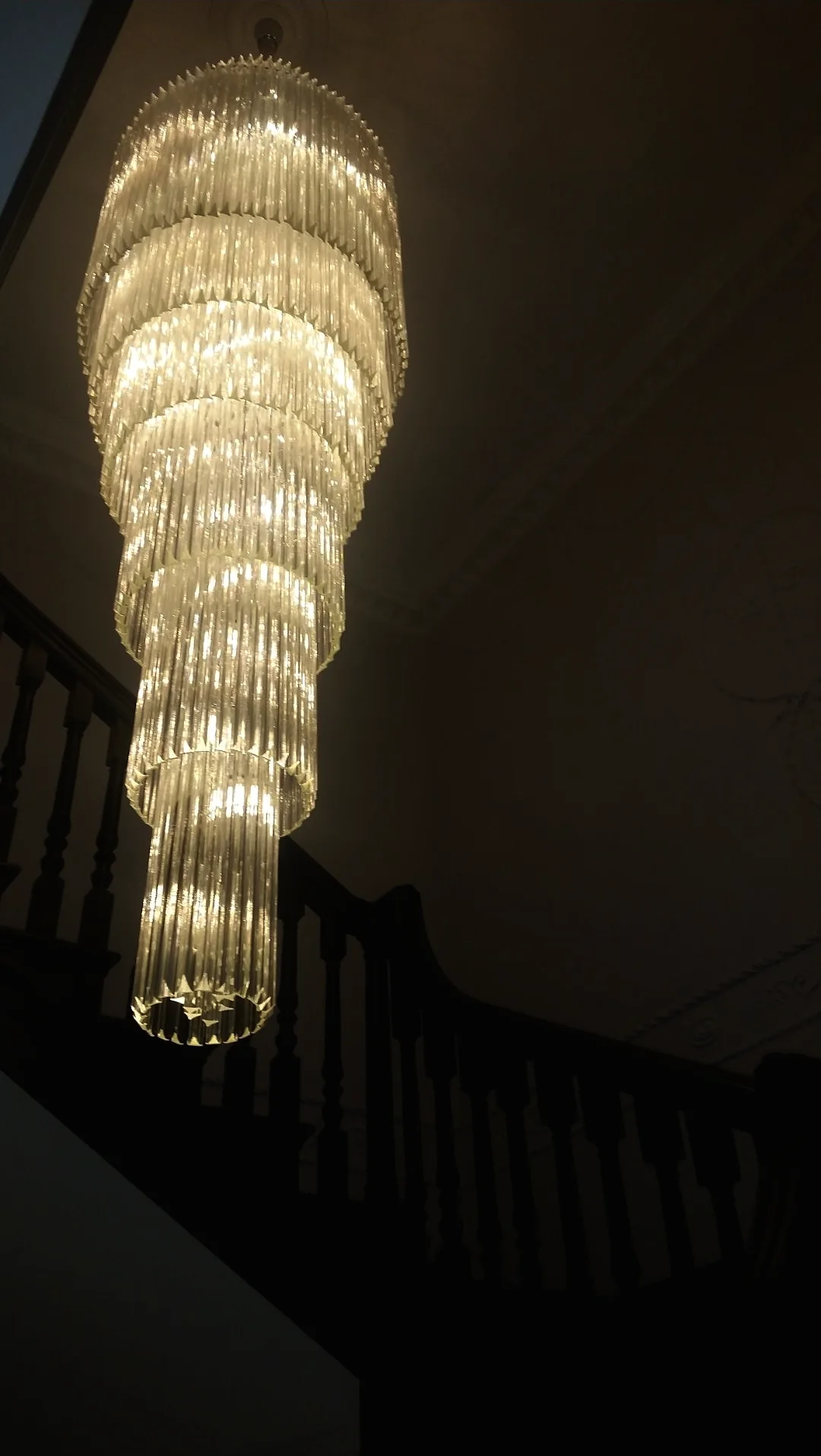 Illuminated tiered crystal tube cascade chandelier in a dark stairwell