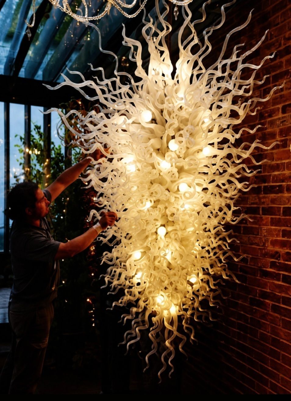 Specialist working beside a large white glass chandelier against a brick wall