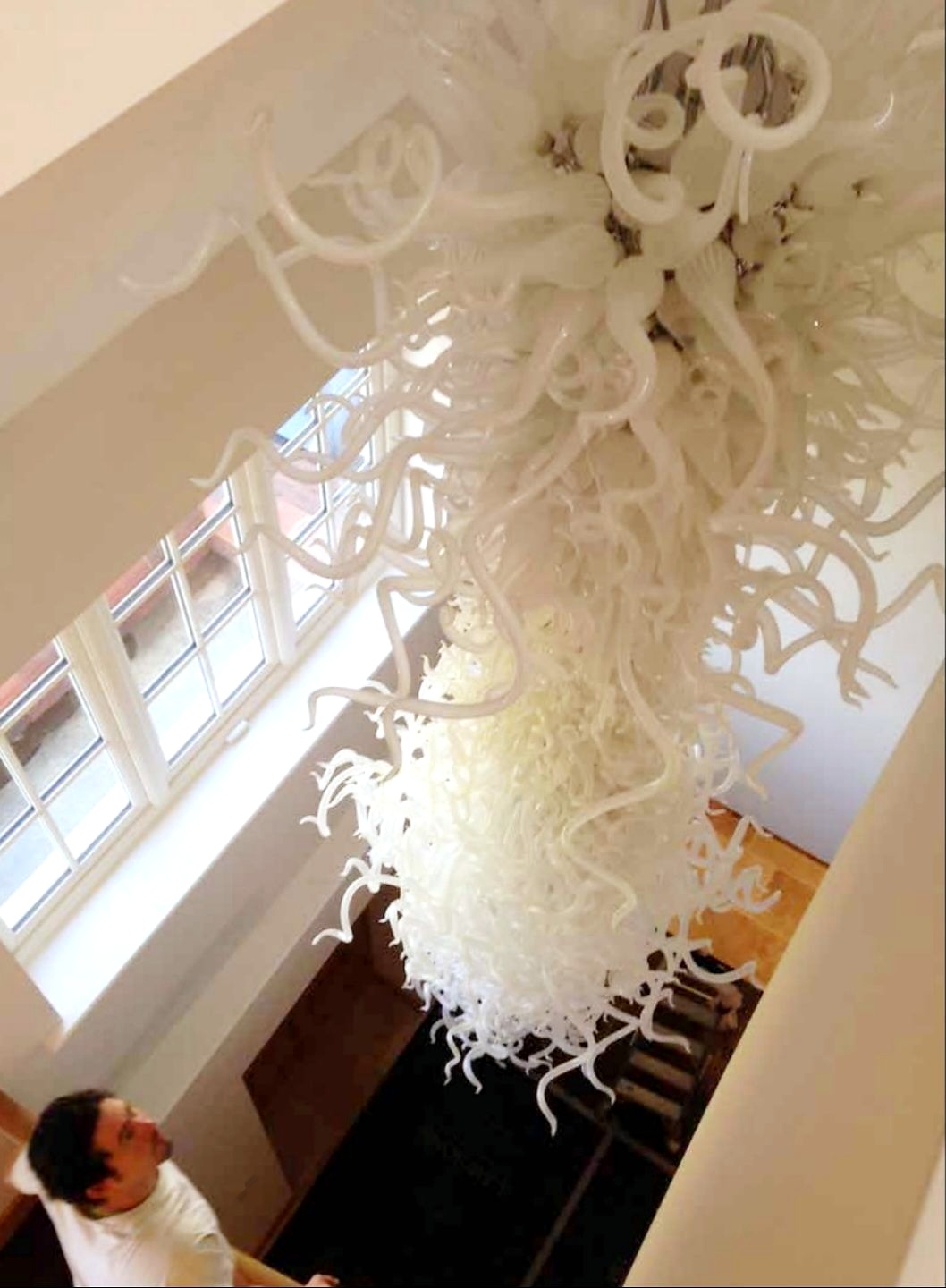 White hand-blown glass tendril cascade chandelier suspended in a bright stairwell